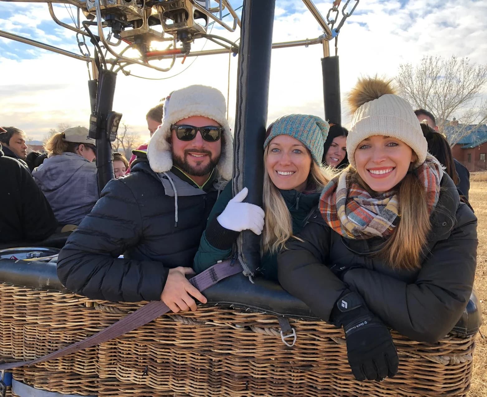 Three smiling passengers leaning over the side of a balloon basket
