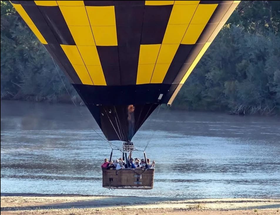 A yellow and navy hot-air balloon flying low over the Rio Grande