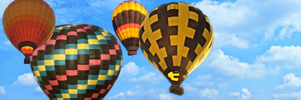 Four hot air balloons rise into a bright blue sky on a clear day.